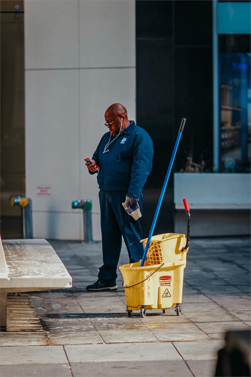 A janitorial worker with a mop and bucket outside a commercial building